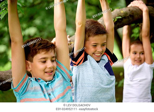 friendship, childhood, leisure and people concept - close up of happy kids or friends hanging on tree and having fun in summer park