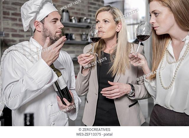 Chef with two women in kitchen tasting wine
