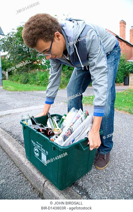 Teenage boy placing curb side recycling collection box on the pavement ready for collection