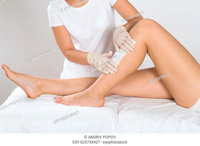 Beautician Waxing Leg Of Woman With Wax Strip At Beauty Clinic