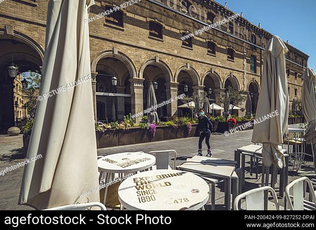 24 April 2020, Spain, Barcelona: A woman wearing a face mask against the corona virus rolls past closed restaurants in the ""Port Vell""