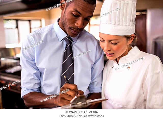 Male manager and female chef writing on clipboard in kitchen