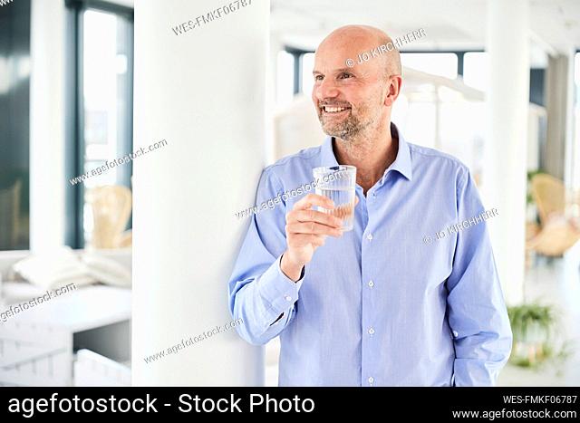 Smiling businessman drinking water while standing at home