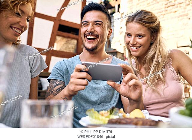 Friends having fun at a barbecue party, taking pictures with their smartphones