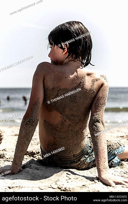 CONEY ISLAND, New York City, NY, USA, 12 years old caucasian teenager boy - with brown hair and in bathing suit at the beach covered in Sand