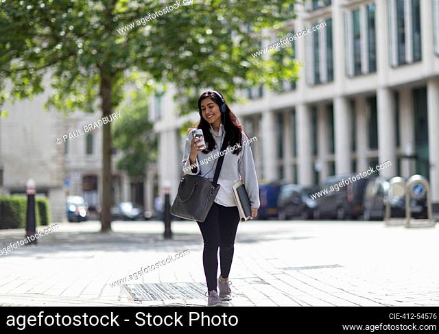 Smiling woman with headphones and smart phone on sunny sidewalk