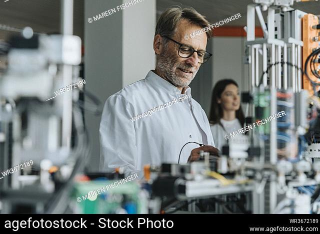 Mature man examining machinery with female colleague in background at laboratory
