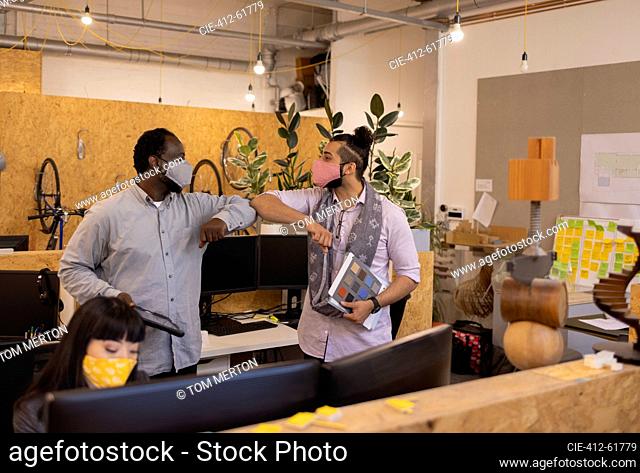 Businessmen in face masks elbow bumping in office