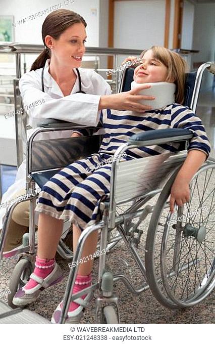 Female doctor adjusting childs neck brace in wheelchair in hospital corridor