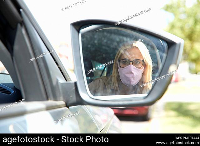 Reflection of woman wearing protective face mask sitting in car