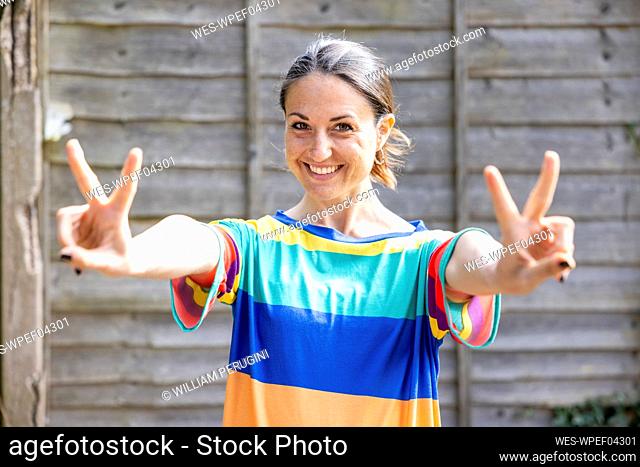 Smiling beautiful woman showing peace sign standing in front of wall