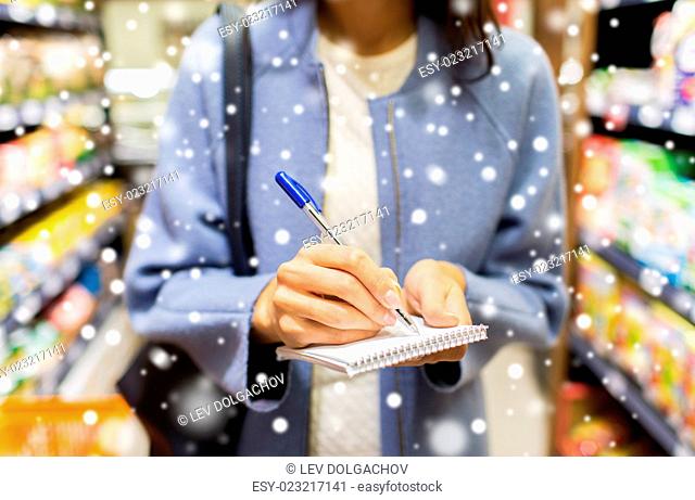 sale, shopping, consumerism and people concept - close up of young woman with pen taking notes to notebook in market over snow effect