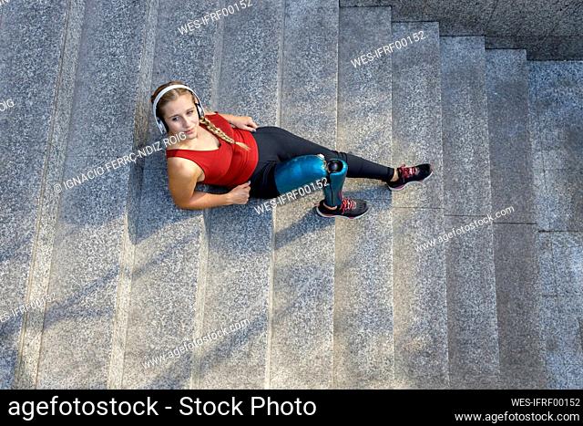 Young sportswoman with prosthetic leg relaxing while sitting on steps