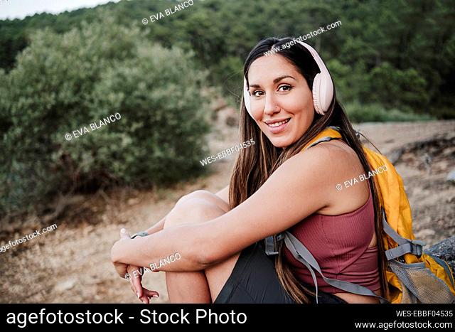 Smiling woman listening music through wireless headphones while hiking in forest