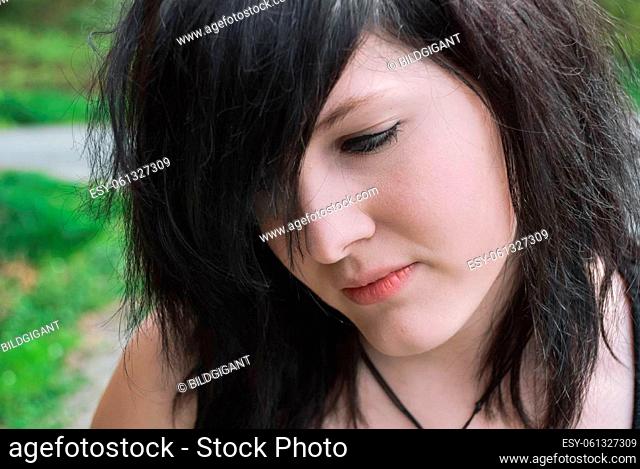 Gothic emo girl looking down with thoughtful facial expression, black hair, close-up