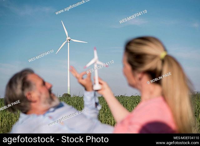 Woman holding windm turbine model sitting with man in field