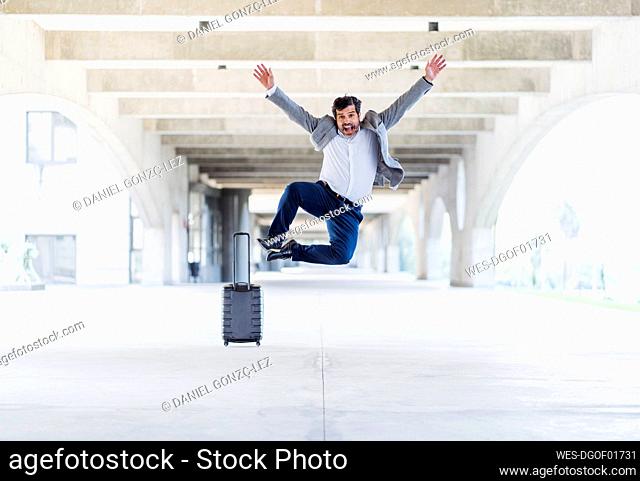 Happy male entrepreneur jumping with hands raised over concrete footpath