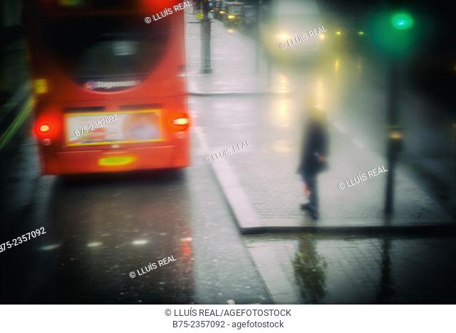 View of a wet street in a rainy day with a double decker bus, unrecognizable man on the sidewalk and a green traffic light in London, England, UK, Europe