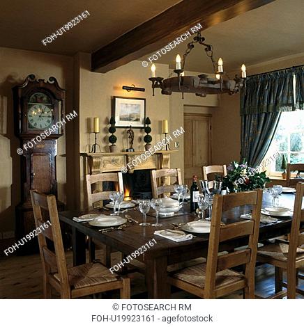 Wrought iron chandelier above rectangular table with place settings in cottage dining room with longcase clock beside fireplace