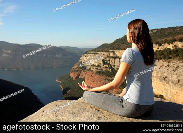 Woman doing yoga on the top of a cliff