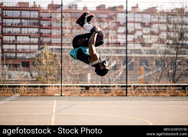Young man practicing acrobats on sports court during sunny day