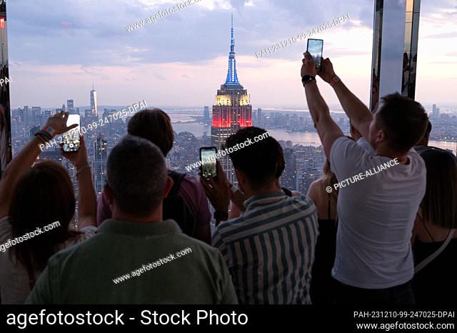 04 September 2023, USA, New York: Visitors photograph the Empire State Building at sunset from the glazed viewing platform The Summit at One Vanderbilt