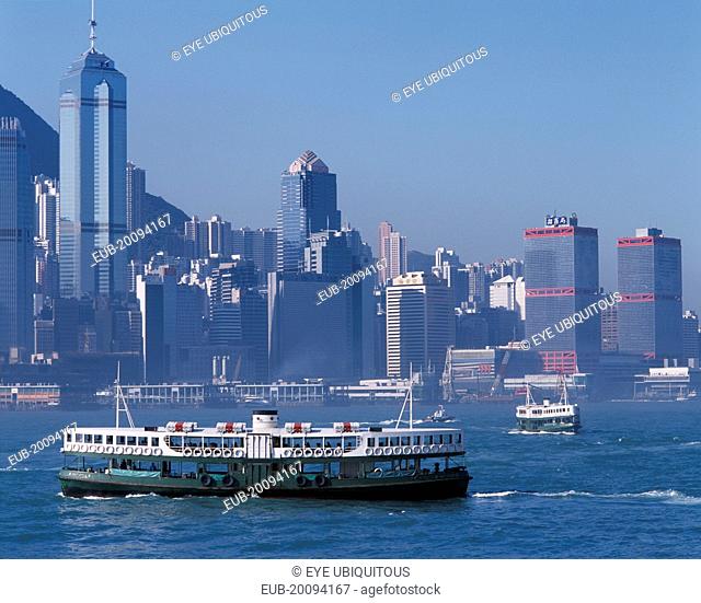 Star Ferries crossing Victoria Harbour with high rise buildings on city skyline beyond