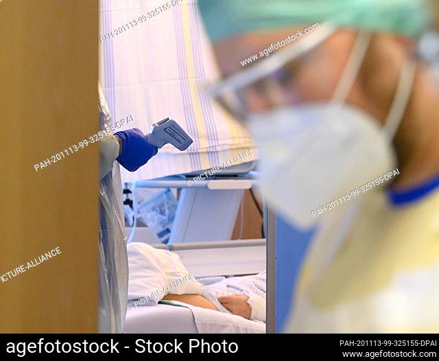 13 November 2020, Saxony, Dresden: A nurse holds a digital fever meter in his hand in the corona emergency room of the Dresden University Hospital while a...