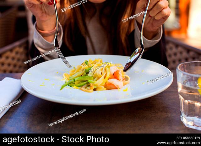 Close up of a plate of fettuccine pasta topped with shrimp. Woman eating at the table