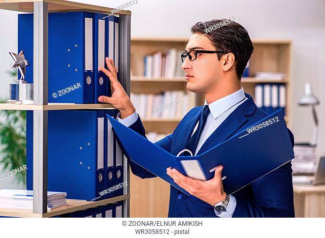 Young man standing next to the shelf with folders