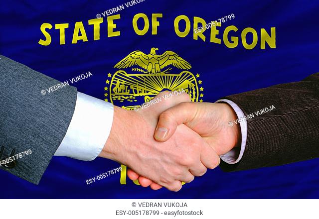 in front of american state flag of oregon two businessmen handsh