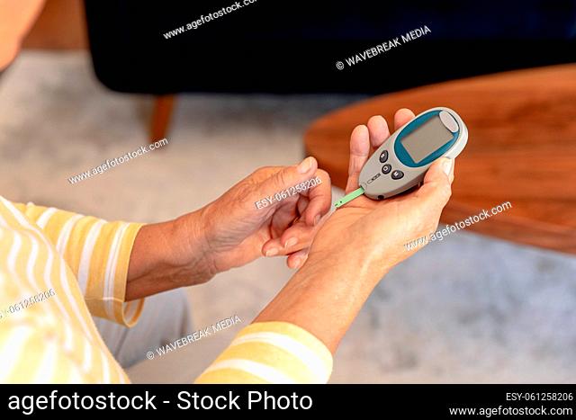 Mid section of caucasian senior woman measuring her blood sugar using glucometer at home