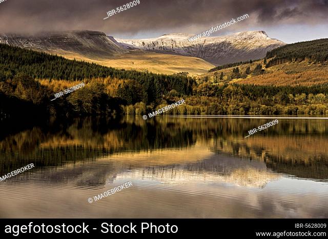 Trees and snow-capped hills reflected in the reservoir at sunrise, Penyfan and Corn Du, Taf Fechan Reservoir, Brecon Beacons N. P