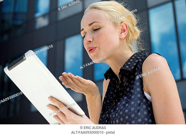 Young woman blowing kiss at digital tablet