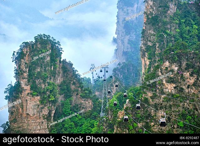 Famous tourist attraction of China, Zhangjiajie stone pillars cliff mountains in fog clouds with cable railway car lift at Wulingyuan, Hunan, China