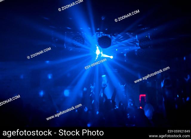 View of a party with bright disco ball sphere, people dance and raise hands