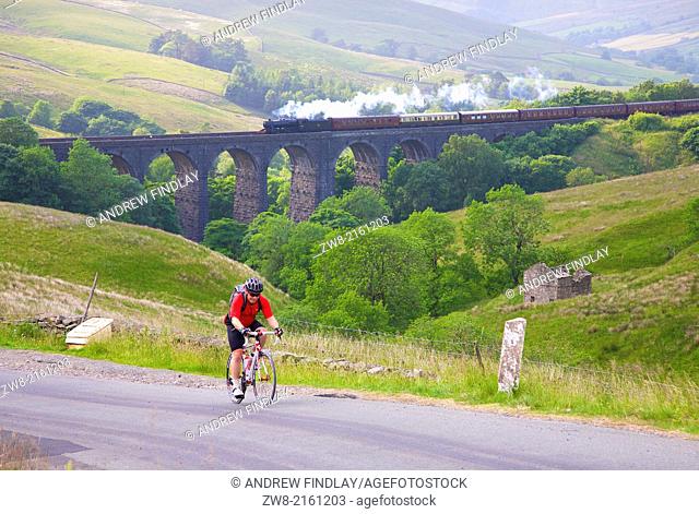 Cyclist in front of viaduct with steam train LMS Stanier Class 8F ""Fellsman"" 48151, pulling carriages on Dent Head Viaduct Yorkshire Dales National Park North...