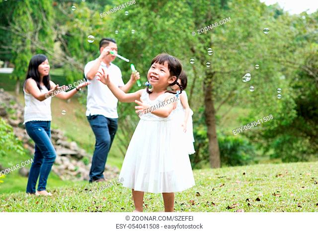 Parents and children blowing soap bubbles at park. Asian family outdoors activity
