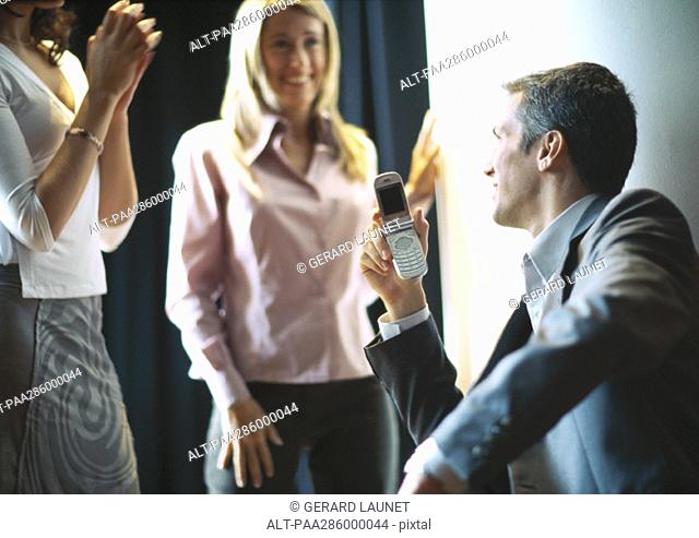 Businessman holding up cellphone, female colleagues smiling and clapping