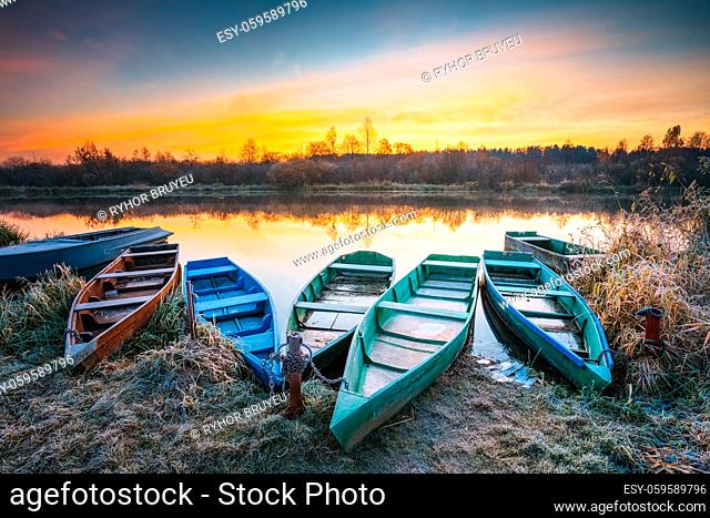 Lake, River and rowing fishing boat at beautiful sunrise in autumn morning. Old wooden boats and frosted grass