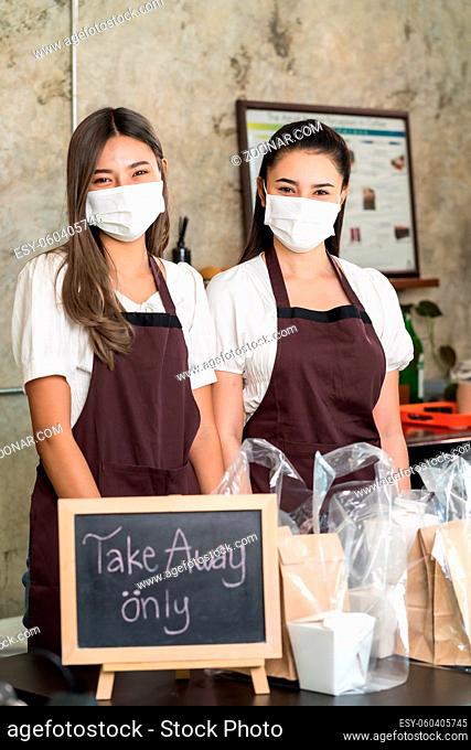Portrait of waitress wear protective face mask smiling with take away or takeout food sign. This essential service is very popular while city lockdown from...
