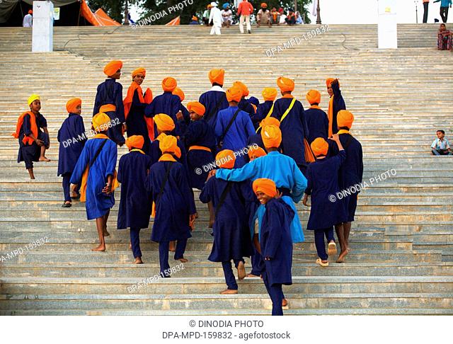 Group of young Sikh boys in blue clothes with saffron head-gear climbing stairs of Sachkhand Saheb Gurudwara ; 300th year of Consecration of  Guru-Granth Sahib...