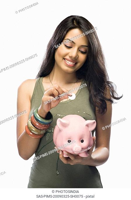 Young woman putting a coin into a piggy bank