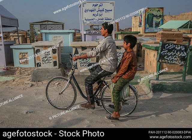 12 November 2020, Iraq, Najaf: Children ride a bicycle through Wadi al-Salam (Valley of Peace) cemetery in the Shiite holy city of Najaf