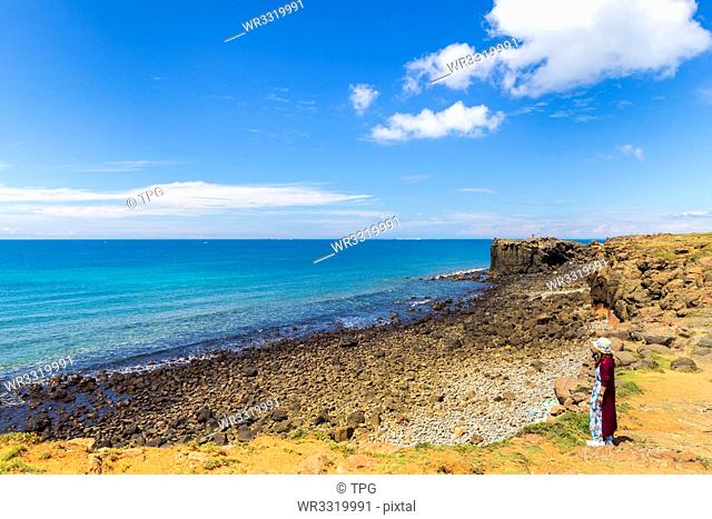 Girl in red.Blue ocean and sky with white cloud beside the coast;hale Cave;Xiaomenyu;Penghu;Taiwan