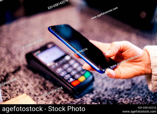 Closeup view hand holding smartphone near pos terminal while paying at cafe or restaurant. New easier and faster contactless technologies of paying
