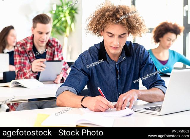 Portrait of a young hard-working student sitting at desk while writing during class in a modern college or university
