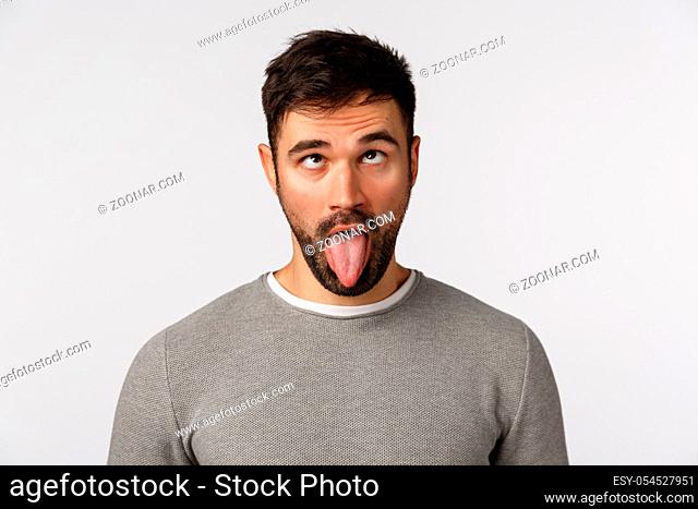 Close-up studio shot funny bearded guy going crazy home-sick home, showing tongue and roll eyelids upwards as making goofy, playful expression