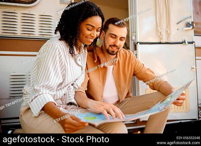 Love couple looking on map near rv, camping in a trailer. Man and woman travels on van, romantic vacations on motorhome, campers leisures in camping-car