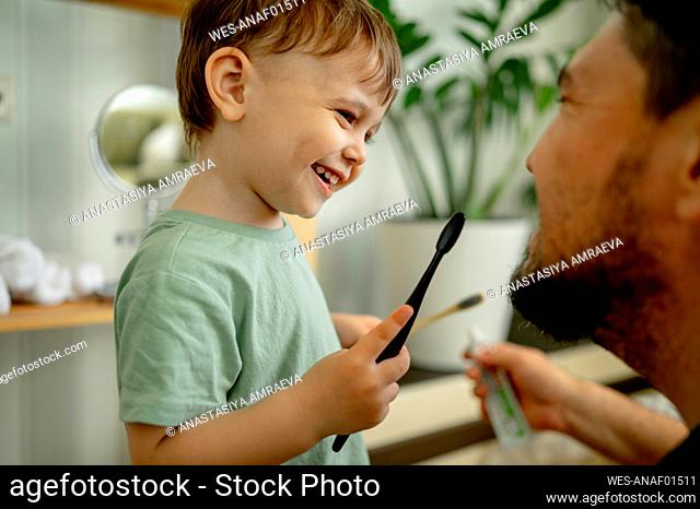 Happy man with boy holding toothbrush at home